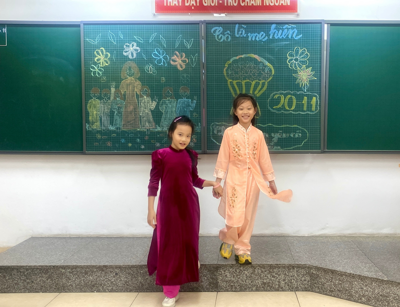 Two girls in dresses holding hands in front of a chalkboard

Description automatically generated