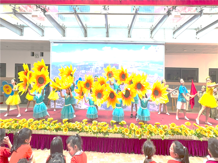 A group of children performing on a stage with yellow flowers

Description automatically generated
